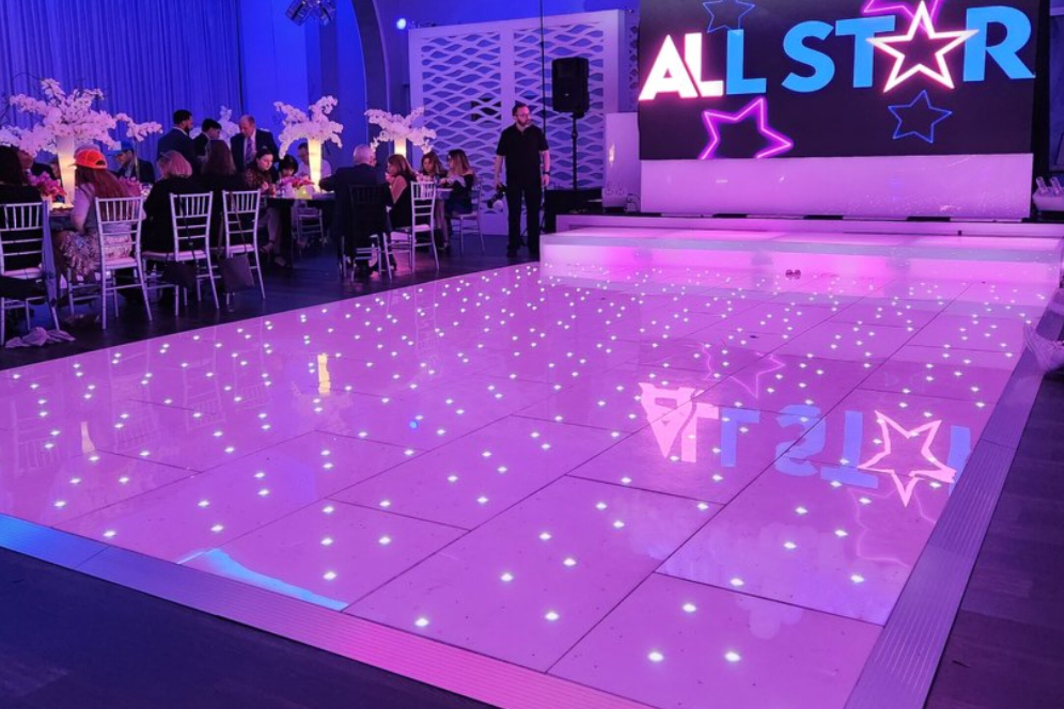 A mesmerizing infinity mirror dance floor illuminated in pink, set in a spacious and elegantly decorated tent.