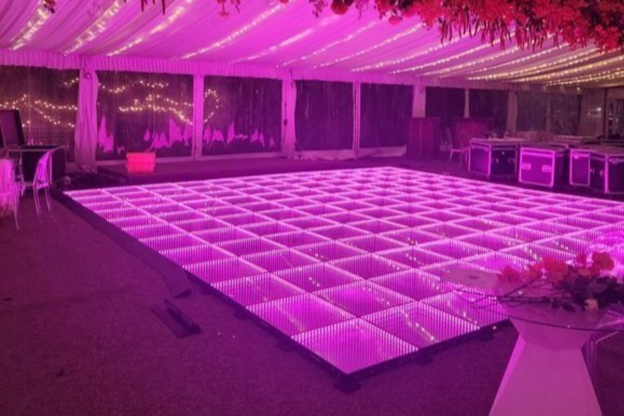 A mesmerizing infinity mirror dance floor illuminated in pink, set in a spacious and elegantly decorated tent.