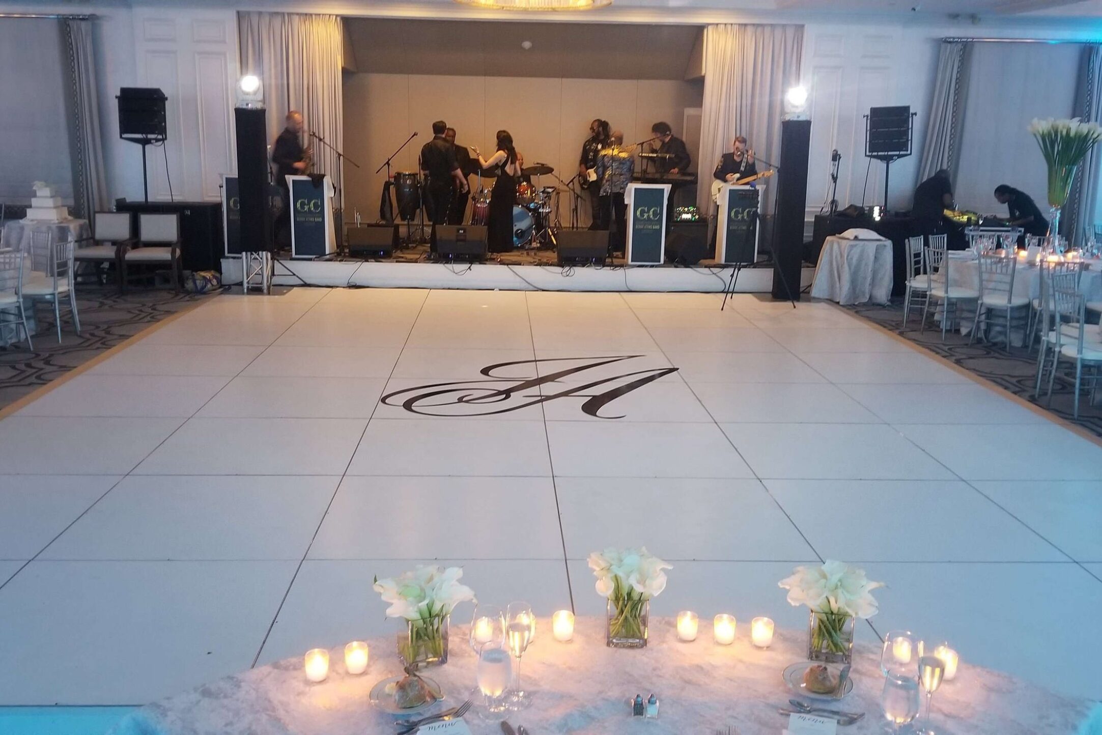 A sophisticated white dance floor with a monogrammed design, set before a live band stage at an elegant indoor venue.