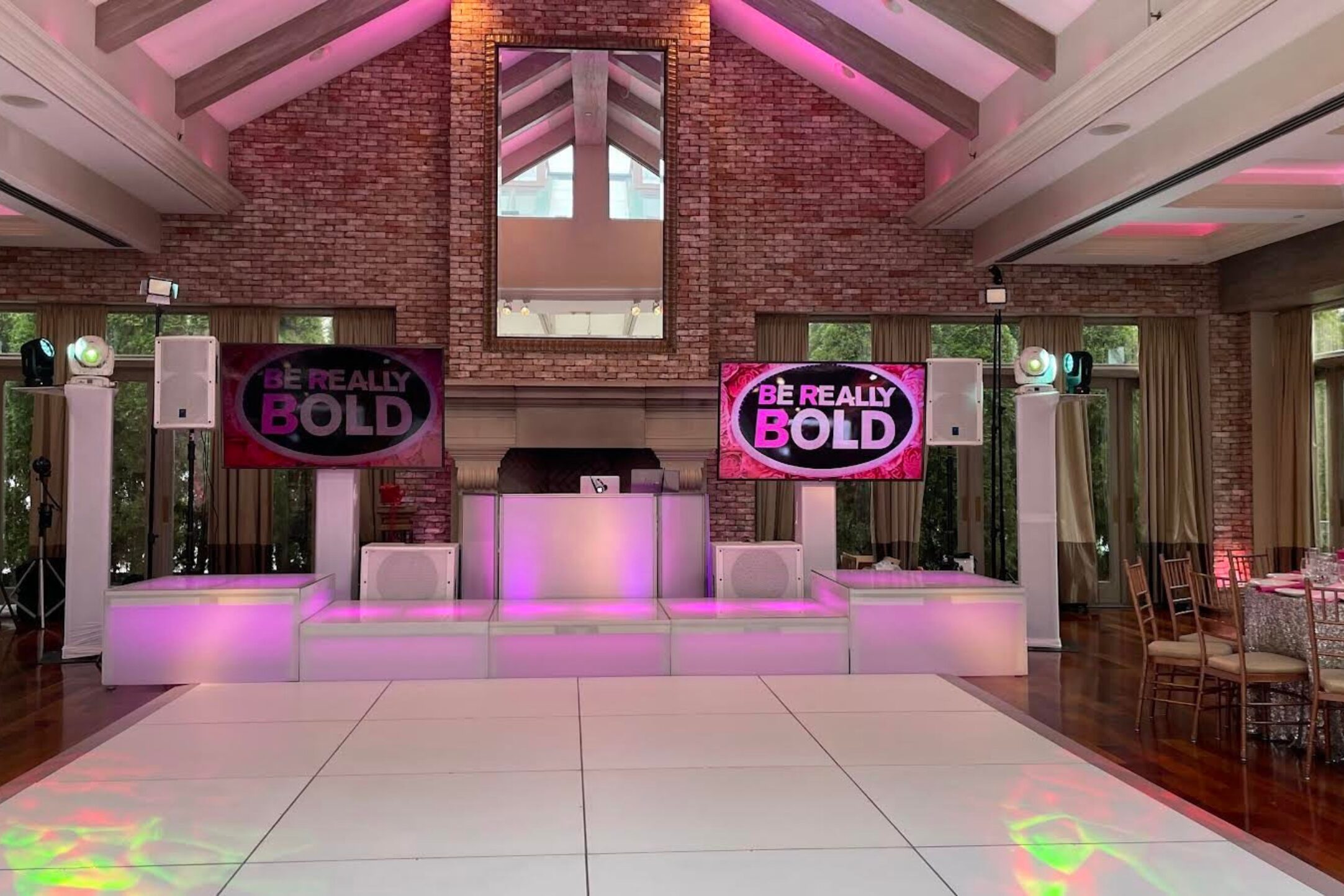 A modern and vibrant indoor DJ setup featuring sleek LED screens displaying "Be Really Bold" and a polished white dance floor.