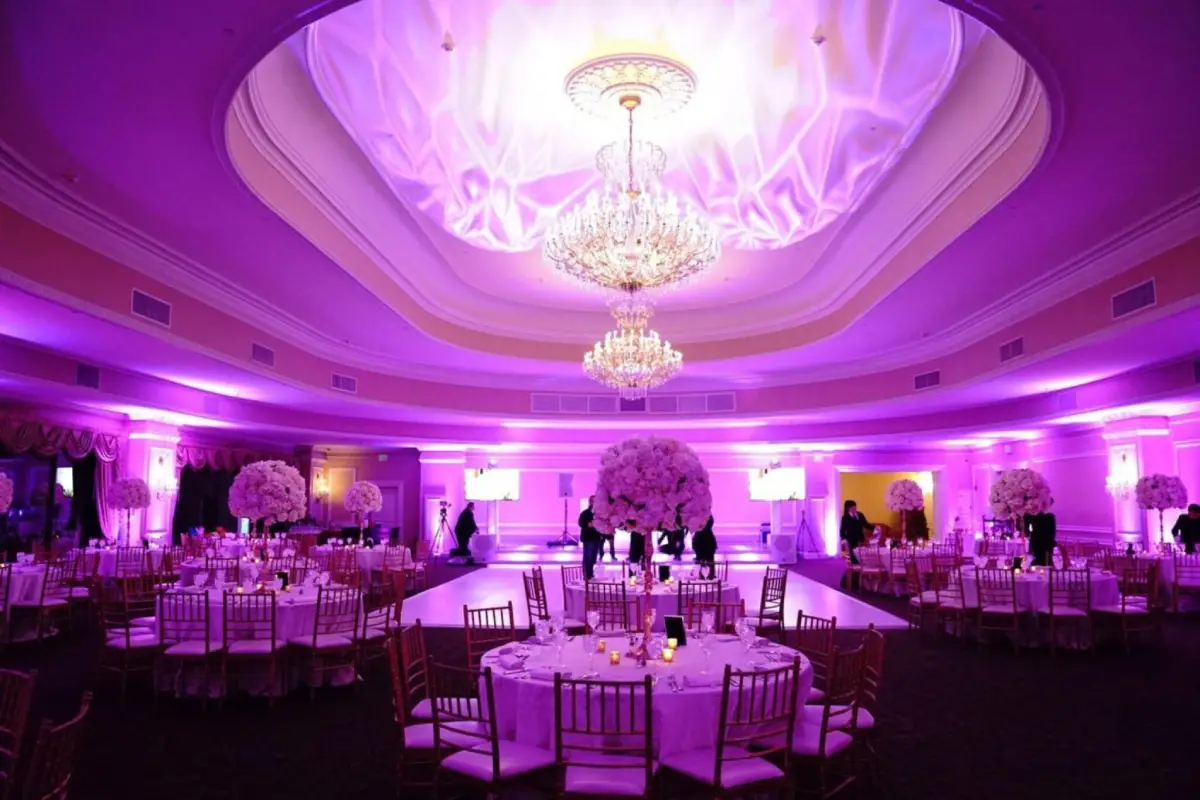 Lavish ballroom illuminated with purple uplighting, featuring crystal chandeliers and elegant table settings.