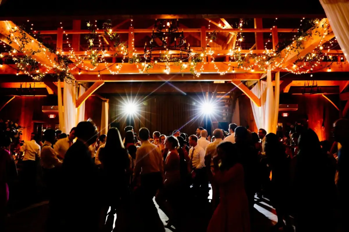 Guests dancing under warm, glowing string lights in a rustic barn venue, creating an enchanting atmosphere.