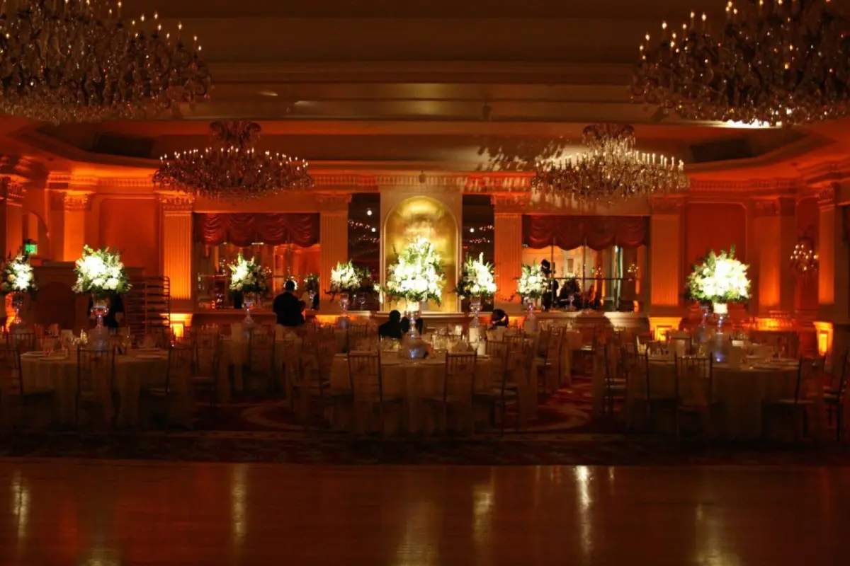 Luxurious ballroom with warm ambient lighting, decorated with white floral arrangements and chandeliers, creating an opulent atmosphere.